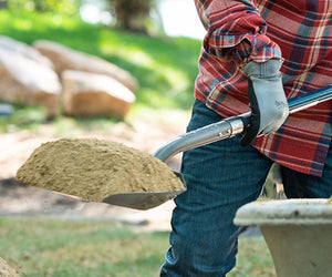  A person moving sand with a shovel out of a wheelbarrow, possibly gardening or excavating while wearing work gloves.