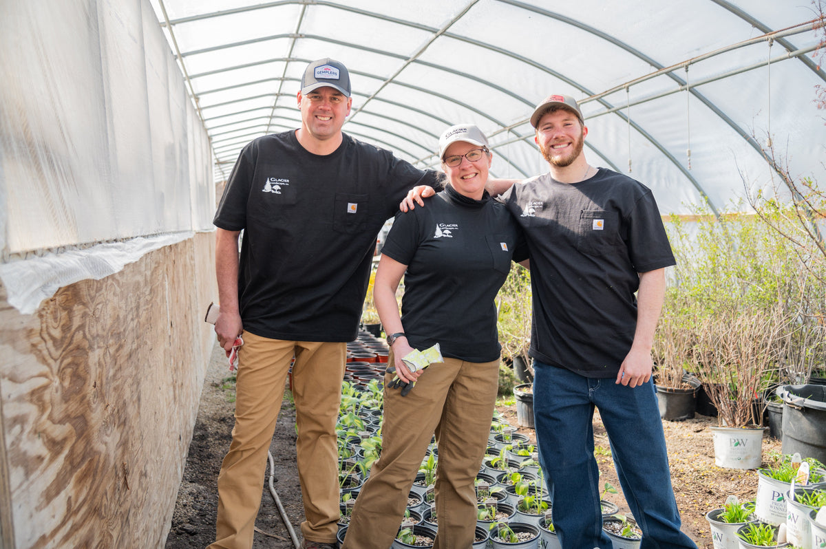 Three people posing together in a greenhouse wearing custom embroidered workwear.