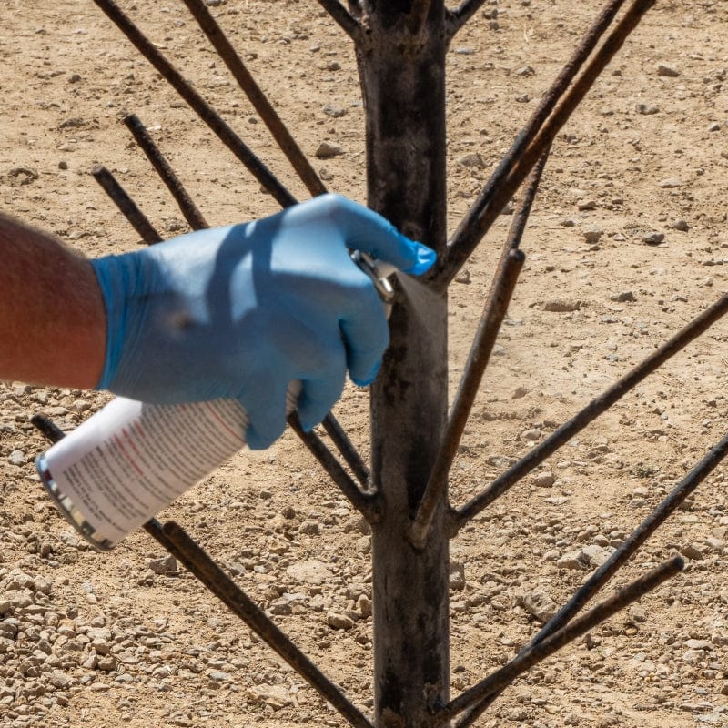 Commercial farmer wearing nitrile gloves to spray rust converter on a milk bottle drying rack.