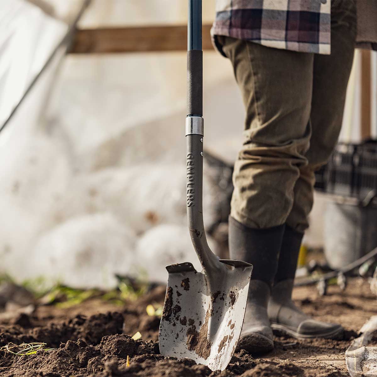 A person digging in the dirt with a shovel from Gemplers, possibly gardening or excavating while wearing chore boots.