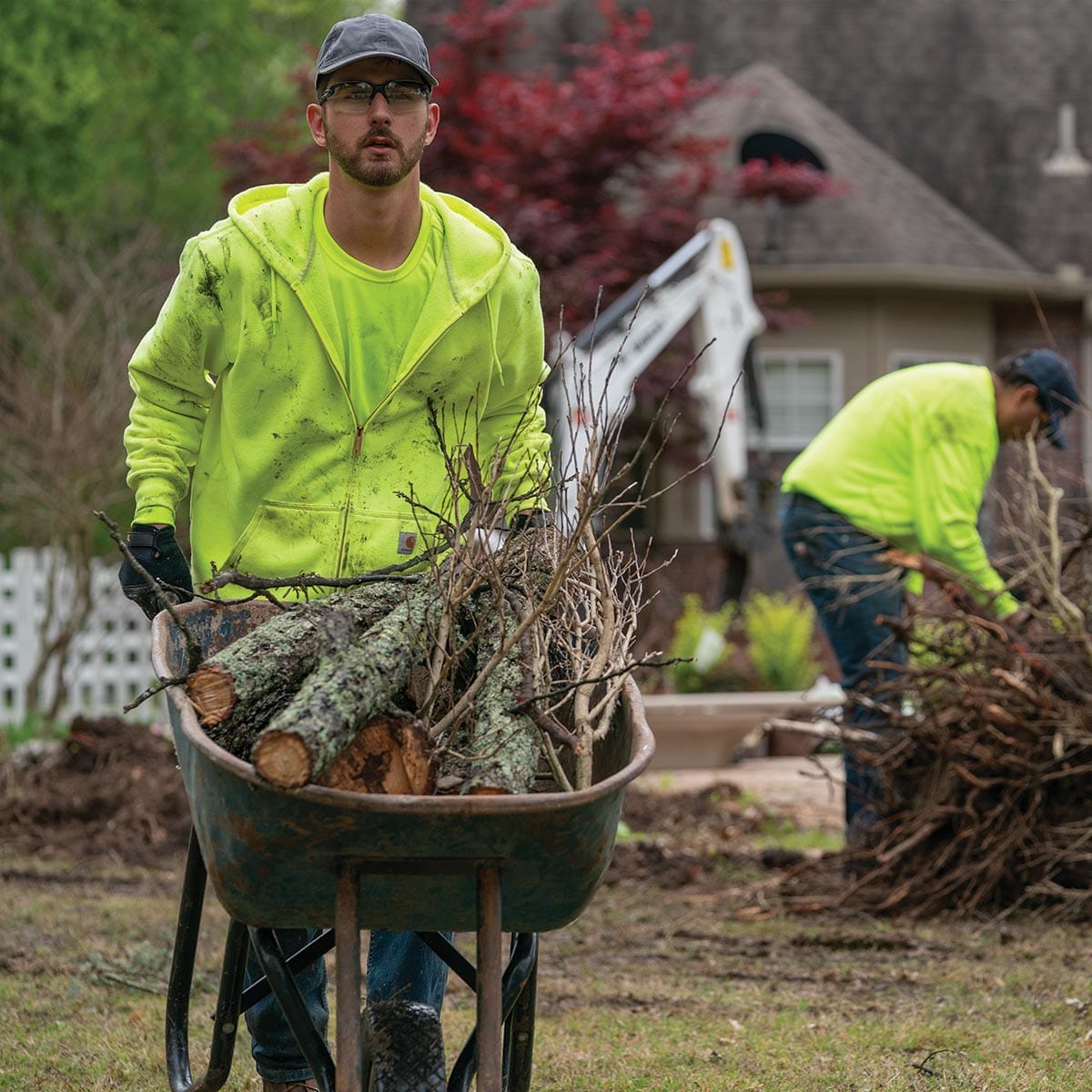 Man wearing Carhartt K122 and pushing wheelbarrow doing yard cleanup