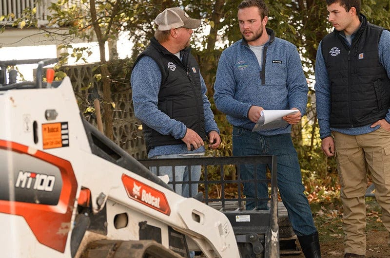 3 men standing by skid steer