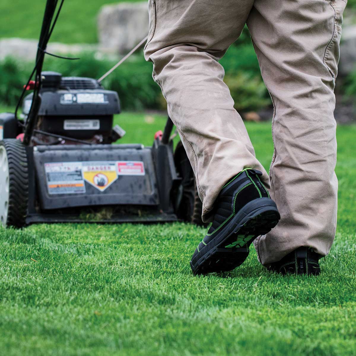 Person wearing black and green Kujo Yardwear Yard Shoes while mowing a lawn